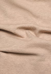 Beige gestrickter Stoff mit feiner Textur und weichem Fall, versehen mit einem gerippten Saum. Keine deutlichen Muster oder Beschläge vorhanden.