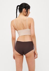 Vaalea beige ribbattu bralette ohuilla olkaimilla yhdessä tummanruskeiden keskikorkeiden alushousujen kanssa, näyttäen sileää kangasta ja yksinkertaista muotoilua.