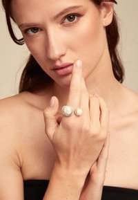 Anillo de plata con dos perlas de diferentes tamaños, exhibido de manera destacada en un dedo. Textura suave contra un fondo neutral.