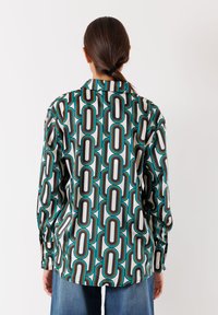Camicia a maniche lunghe in tessuto leggero con motivo geometrico nei colori turchese, nero e bianco. Colletto classico e polsini con bottoni.
