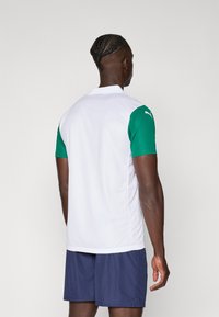 Bijela sportska polo majica s kratkim zelenim rukavima, koja ima ovratnik i brendirani logo na ramenu. Nosena je s tamnoplavim kratkim hlačama.