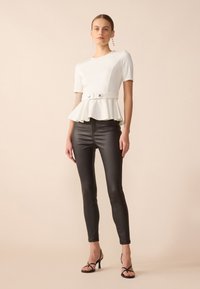Hvit peplum-top med korte ermer, belte i midjen og to knapper, kombinert med skinnende svarte tettsittende bukser og strømpehæler.