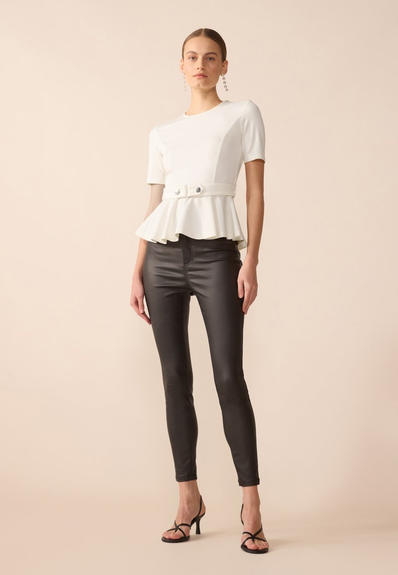 Weißes Peplum-Top mit kurzen Ärmeln, das eine taillierte Taille und zwei Knöpfe hat, kombiniert mit glänzenden schwarzen, eng anliegenden Hosen und Riemchen-Heels.