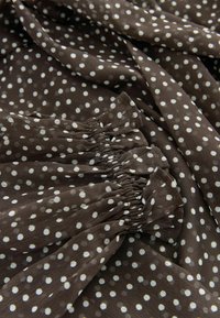 Pruunide täppidega kangas valgete täppidega; pehme, kerge materjal; varrukal on koondatud elastne osa tekstuurse välimuse saavutamiseks.