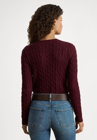 Μπορντό πουλόβερ με πλεκτό σχέδιο, άνοιγμα λαιμού τύπου crew, μακριά μανίκια και υφασμένο μοτίβο, συνδυασμένο με ψηλόμεσα μπλε τζιν και καφέ ζώνη.