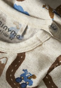 Bebiskläder i mjuk, beige bomull; har blå och bruna mönster av fordon och vägar. Inkluderar tryckknappar vid halsen.