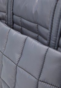 Veste grise rembourrée avec une texture matelassée, dotée d'une finition lisse et brillante ainsi que de coutures bien réalisées.
