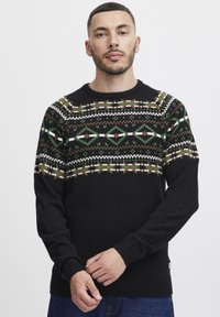 Pulover negru tricotat, cu un model în partea superioară, prezentând designuri geometrice în verde, alb și maro. Mansetele și tivul ribuș oferă un finisaj texturat.