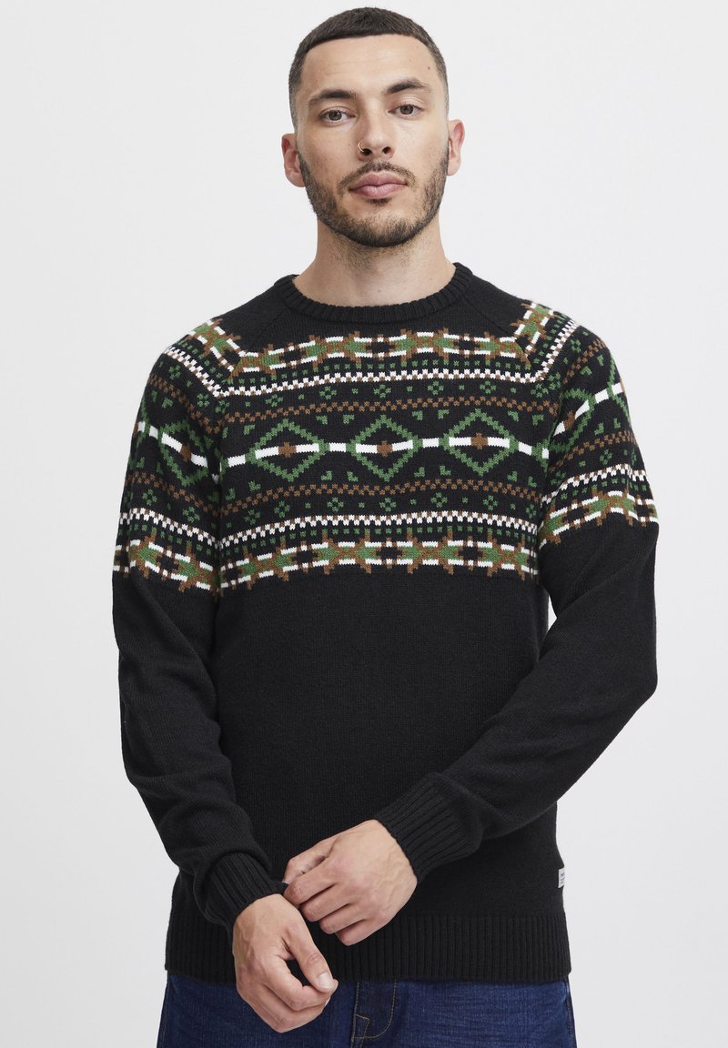 Pulover negru tricotat, cu un model în partea superioară, prezentând designuri geometrice în verde, alb și maro. Mansetele și tivul ribuș oferă un finisaj texturat.