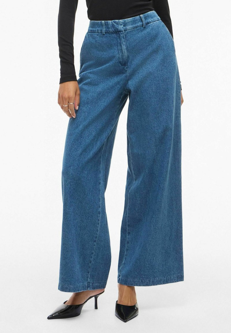 Traprene traperice s visokim strukom i širokim nogavicama, u plavoj boji s laganom izblijedjelom teksturom, s klasičnim dizajnom od pet džepova i prednjim kopčanjem na dugme.