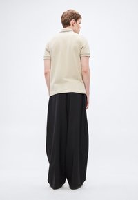 Μπεζ πόλο πουκάμισο με κοντά μανίκια και μαύρο παντελόνι με φαρδιά μπάτ ζώνη. Διαθέτει υφασμένη υφή, αντίθετο γιακά και ρέον ύφασμα.