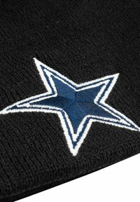 Schwarze Strickmütze mit einem auffälligen blauen Sternmotiv, umrandet mit weißem Faden, das ein strukturiertes Strickmuster zeigt.