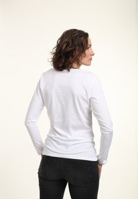 Weißes langärmliges Hemd aus weicher Baumwolle mit rundem Ausschnitt, taillierter Passform und glatter Textur. Kombiniert mit schwarzen Jeans.