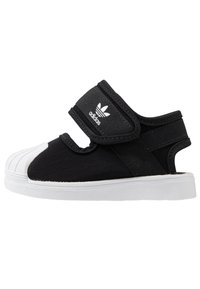 Svarta barndämpare med vit gummitå, Veldroband med Adidas-logotyp och vit sula, öppen häl-design.