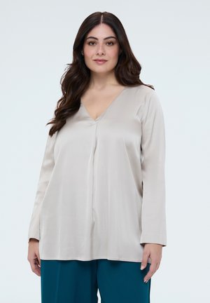 Jasnobeżowa bluzka z długim rękawem i dekoltem w serek, wykonana z gładkiego materiału, z delikatnym drapowaniem i luźnym krojem. Połączona z kontrastowymi spodnie w kolorze teal.
