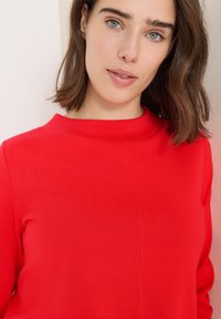 Röd sweatshirt med hög halsringning, med en slät textur och en enkel, ren design. Inga synliga mönster eller hårdvarudetaljer.