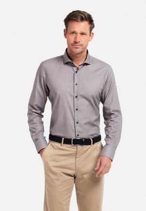 Chemise à manches longues pour homme en gris clair avec de petits pois noirs, boutonnée, coupe ajustée, avec un col. Pantalon beige et ceinture noire.