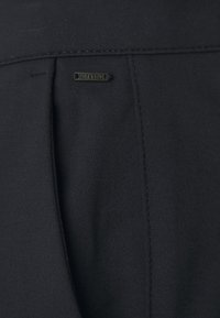 Zwarte stof met een gestructureerd oppervlak, voorzien van een verticale naad en een klein metalen label met "Black & Blue" in reliëf geschreven.