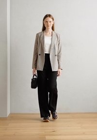 Blazer rayé, haut blanc, pantalon large noir, baskets imprimé animal et petit sac à main noir ; sol en bois clair et fond uni.