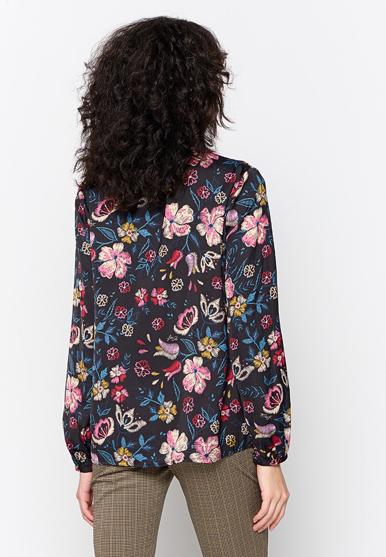 Blusa a maniche lunghe in leggero tessuto nero decorata con motivi floreali colorati. Presenta un collo rotondo e polsini elasticizzati.