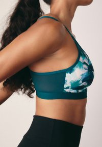 Top sportivo color turchese con una stampa astratta colorata. Presenta un design senza cuciture, spalline regolabili e tessuto traspirante. Leggings neri a vita alta.