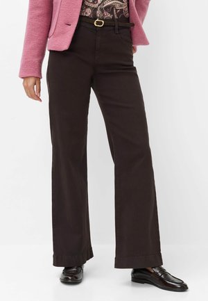 Kvinde iført mørkebrune vidde bukser, sort bælte, sorte loafers, en pink jakke og en mønstret top.