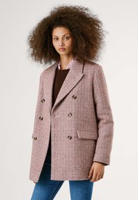 Manteau croisé en motif chevrons rose et blanc, doté de grands boutons, d'un col à revers et de poches latérales. Le tissu semble texturé.