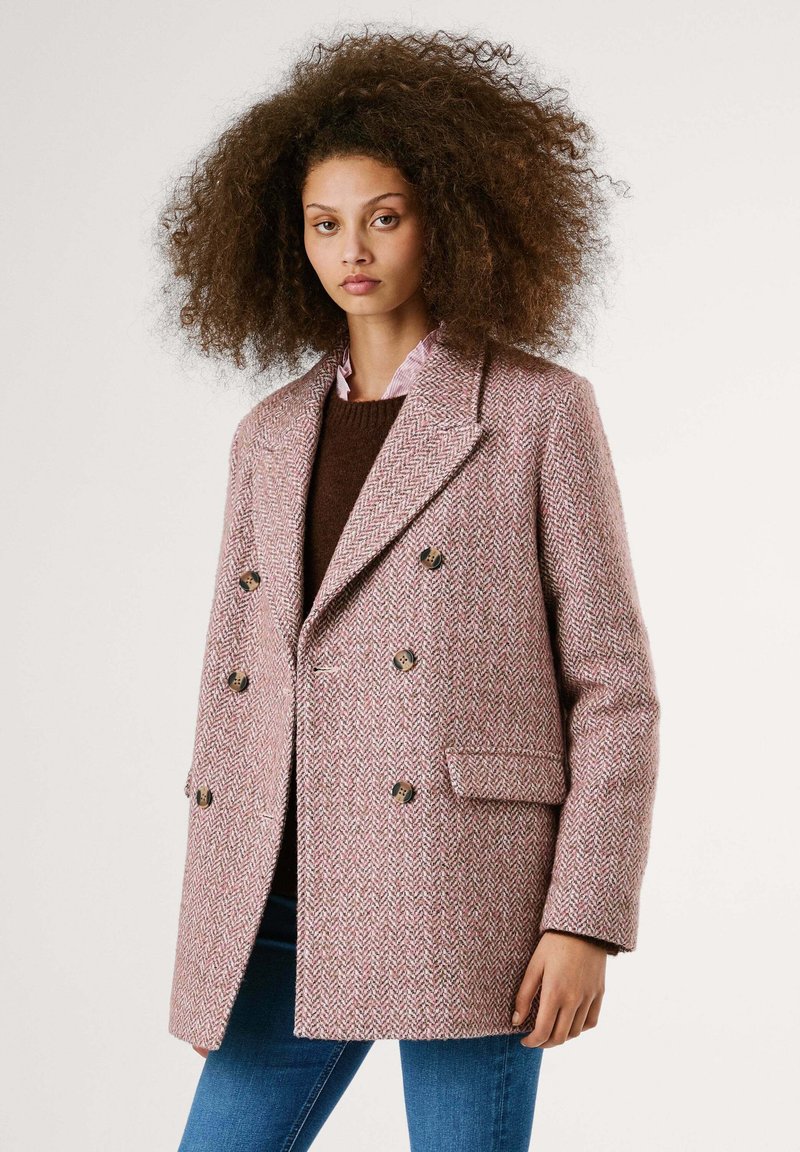 Manteau croisé en motif chevrons rose et blanc, doté de grands boutons, d'un col à revers et de poches latérales. Le tissu semble texturé.