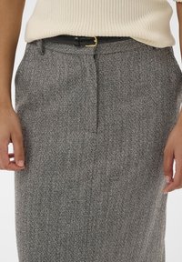 Jupe en tissu à motif chevron gris, avec une fermeture à l'avant, des passants de ceinture et une ceinture noire avec une boucle en or.