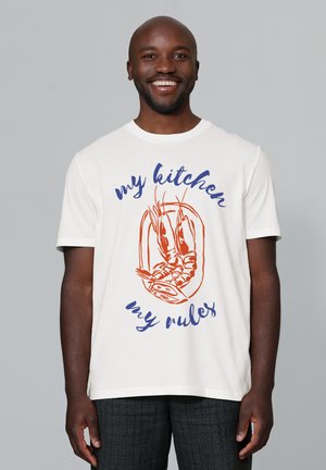 Witte katoenen t-shirt met een kreefoverdruk in oranje en de tekst "mijn keuken mijn regels" in blauw. Korte mouwen, ronde hals ontwerp.