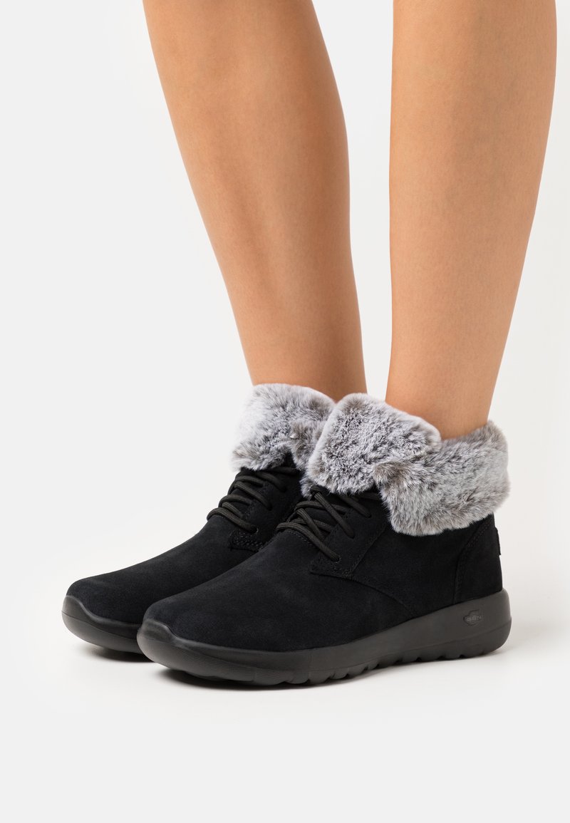 Bottines en daim noir avec des poignets en fausse fourrure grise, bout rond et design à lacets. Semelles en caoutchouc pour plus d'adhérence et de confort.