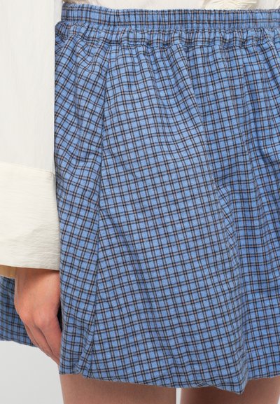 Falda de cuadros azules con una cinturilla fruncida, pliegues y un tejido ligero que presenta un patrón de rejilla de líneas azules y marrones.