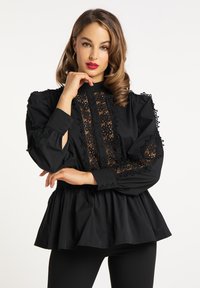 Czarna bluzka z wysokim kołnierzem, koronkowym wykończeniem i bufkami z akcentującymi detalami. Rozkloszowany krój peplum. Materiał: mieszanka bawełny.
