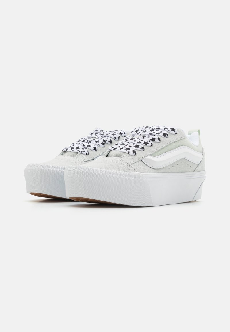Zapatillas de plataforma en gris claro, material de ante, con cordones negros con patrón de estrellas y franjas laterales blancas. Suela de goma texturizada, forro de malla.