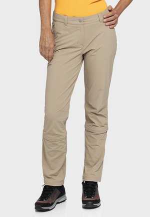 Beige outdoor pants with a slim fit, zippered pockets, and reinforced knees, worn with black and maroon hiking shoes.