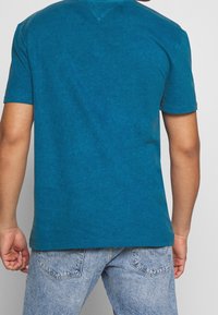 Camiseta de algodón verde azulado con mangas cortas, que presenta una textura sutil y un escote redondeado. Vista trasera mostrando las costuras de los hombros y los detalles del dobladillo.