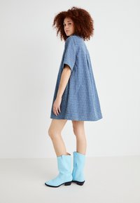 Robe à motifs bleu clair avec des manches courtes, silhouette évasée, associée à des bottes de cowboy hautes bleu clair. Texture de tissu lisse.