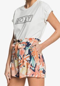 T-shirt blanche avec le logo "ROXY" au-dessus de shorts à motif floral dans les teintes pêche, bleu, vert et jaune. Les shorts ont une taille à nouer et des poches latérales.