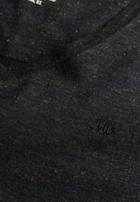 Zwarte gebreide T-shirt stof met gouden sproetjes, voorzien van een subtiele geborduurde logo en een V-halsontwerp. Zachte, gestructureerde uitstraling.