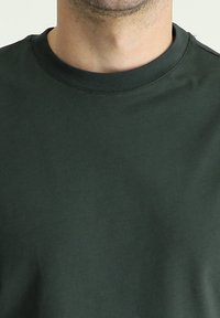 Donkergroene katoenen t-shirt met een ronde hals, een soepele textuur en minimale stikdetails. Geschikt voor casual kleding.