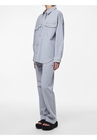 Randig denimskjorta med två framfickor, parat med matchande randiga byxor. Modellen bär svarta platåsandaler. Övergripande ljusblå färg.