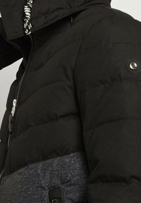 Černá péřová bunda s texturovaným šedým dolním panelem. Obsahuje přední zip, knoflíkové detaily na rukávech a vysoký límec.