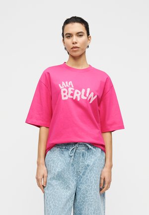 Φωτεινό ροζ υπερμεγέθες μπλουζάκι με το «LALA BERLIN» σε λευκά γράμματα. Απαλό βαμβακερό ύφασμα, στρογγυλή λαιμόκοψη, κοντά μανίκια, σε συνδυασμό με ανοιχτόχρωμο παντελόνι με λεοπάρ σχέδιο.