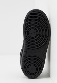 Černá gumová podrážka s kruhovým protiskluzovým vzorem, obsahující logo Nike a text "NEZANECHÁVÁ STOPY". Navrženo pro odolnost a přilnavost.