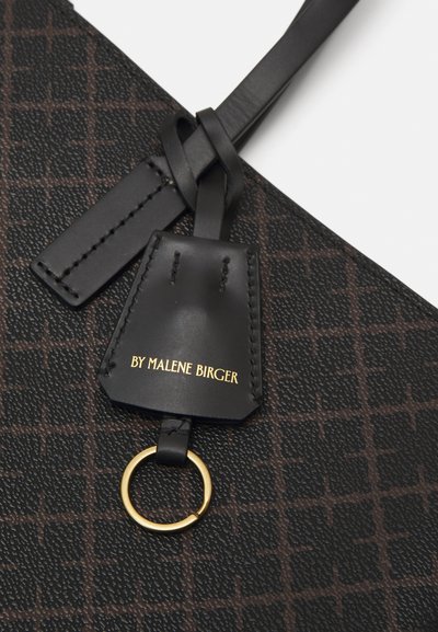 Black bag with a textured surface, featuring a brown grid pattern, woven leather strap, and a tag with gold lettering and a ring.
