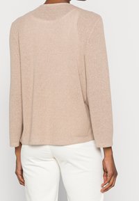 Beige, mjuk stickad tröja med långa ärmar och rundad halsringning, som har ett strukturerat mönster och en avslappnad passform.