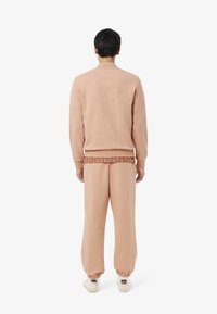 Set di felpa e pantaloni della tuta rosa. La felpa ha un collo rotondo e polsini a costine. I pantaloni sono larghi con polsini elastici e una cintura decorata.