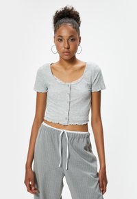 Top corto gris con mangas cortas, textura acanalada, escote de encaje y botón en la parte delantera. Combinado con pantalones grises de rayas y cintura con cordón.
