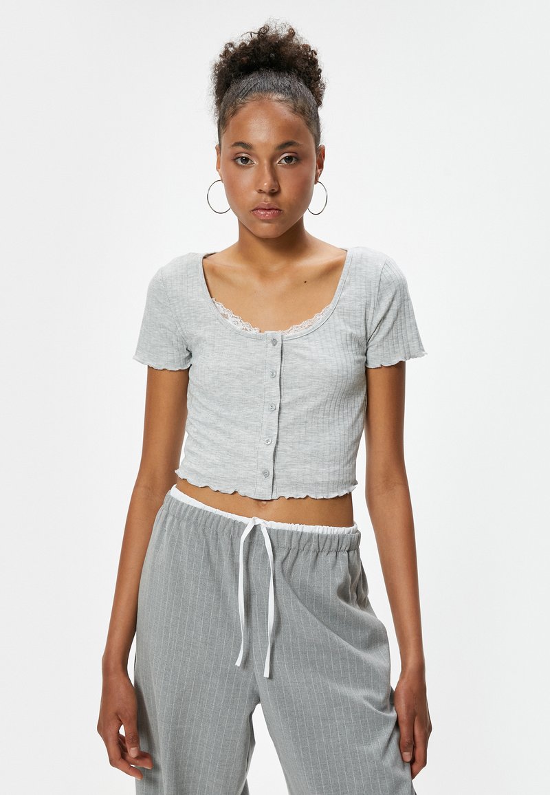 Grå cropped top med korte ærmer, ribbet struktur, blondeudskæring og knaplukning. Hvis du parrer med grå stribede bukser med snoretræk i taljen.