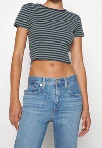 Kortärmad grön och marinrandig t-shirt med rund halsringning, tillsammans med blå raka jeans med fem fickor och denimtextur.